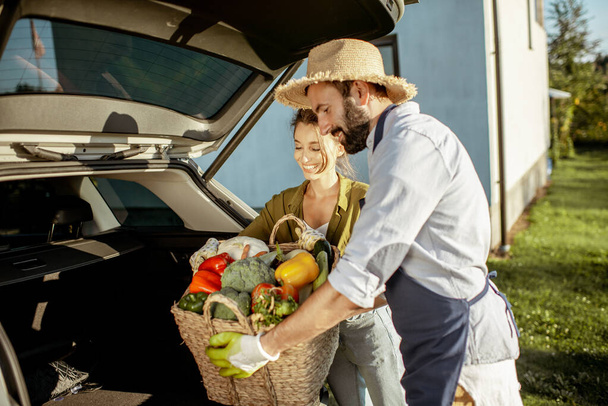 Чоловік і жінка зі свіжими овочами біля машини в сільській місцевості
 - Фото, зображення