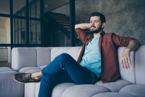 Profile side photo of positive cheerful guy have rest relax after finished work sit on comfy divan dreaming feel content wear casual style clothing in house loft - Фото, зображення