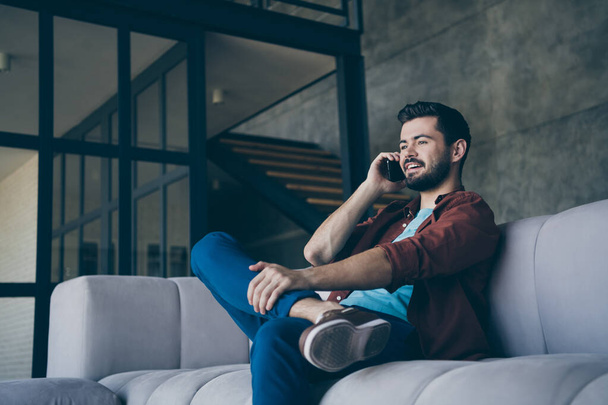 Profile photo of handsome guy holding telephone near ear listening foreign friend chatterbox cosy sit sofa in living room modern apartment indoors casual dressed - Fotoğraf, Görsel