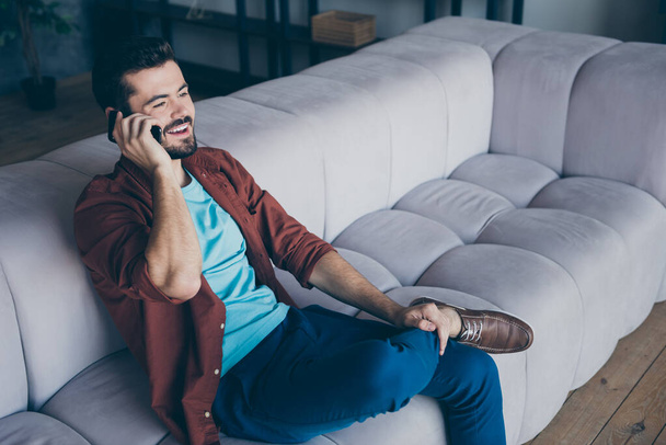 Profile photo of handsome guy holding telephone near ear listening foreign friend chatterbox cosy sit sofa in living room modern apartment indoors casual dressed - Fotoğraf, Görsel