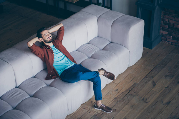 High angle above view photo of handsome guy in high spirits holding hands behind head sitting couch relaxing saturday morning in modern flat indoors - Foto, imagen