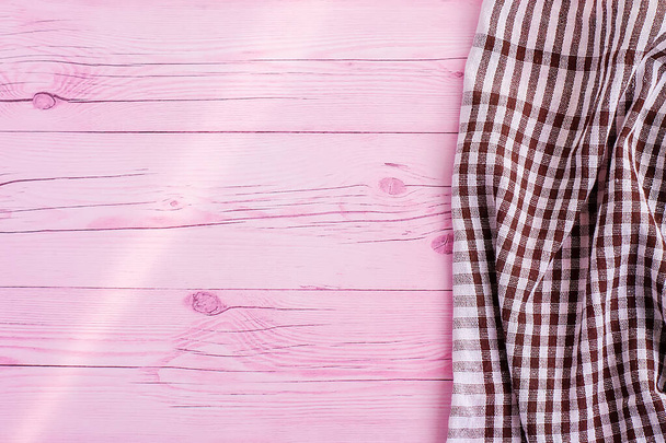 ピンク色の木製のテーブルの上には、白と茶色のチェッカーキッチンタオルや綿のナプキンがあります。上からの眺め。テキストのスペースをコピーします。デザインのレイアウトとして使用できます。料理の背景 - 写真・画像
