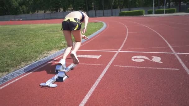 Štíhlá mladá dívka sportovec začít utíkat z bloku na stadionu. Zpomalený pohyb, stálý výstřel - Záběry, video