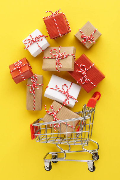 Shopping cart full of gift boxes on yellow background. - Фото, изображение