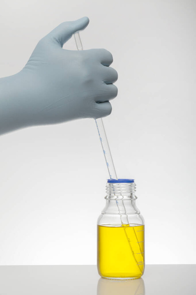 Una mano en guantes de laboratorio mezcla química. Líquido en botellas de laboratorio. Laboratorio científico bioquímico. Colorido líquido
. - Foto, imagen