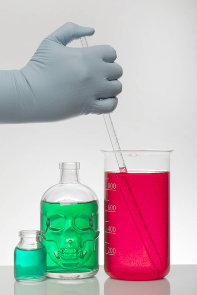 Laboratuvar eldivenlerindeki bir el kimyayı karıştırır. Laboratuvar şişelerinde sıvı. Bilimsel biyokimya laboratuvarı. Renkli sıvı. - Fotoğraf, Görsel