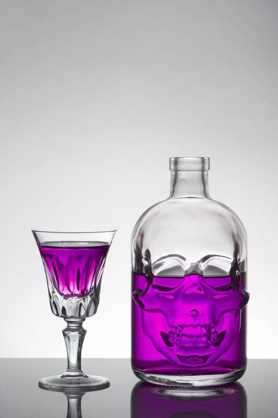 Láhev lebky a křišťálové sklenice s tekutinou, alkoholický nápoj. - Fotografie, Obrázek
