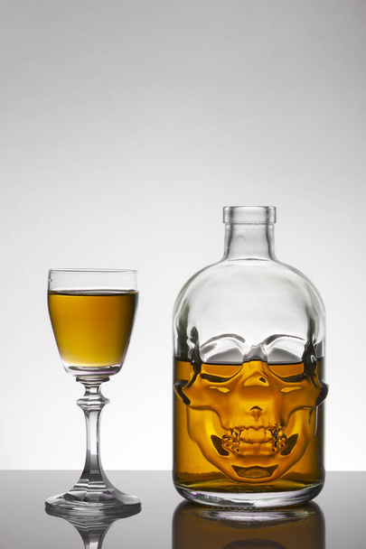 Ένα μπουκάλι κρανίο και κρυστάλλινα ποτήρια με ένα υγρό, αλκοολούχο ποτό. - Φωτογραφία, εικόνα