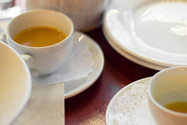 weiße Tassen mit gelbem Sandhorntee auf hölzernem Tisch unterlegt von Geschirr, selektiver Fokus - Foto, Bild