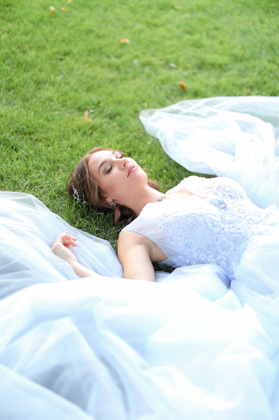Innocent beautiful bride lying on grass in oark and wearing white dress. - Foto, immagini