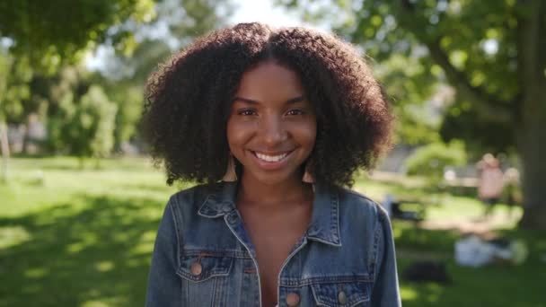 Portrait of an young african american woman standing in the park smiling and looking into camera  - Video, Çekim