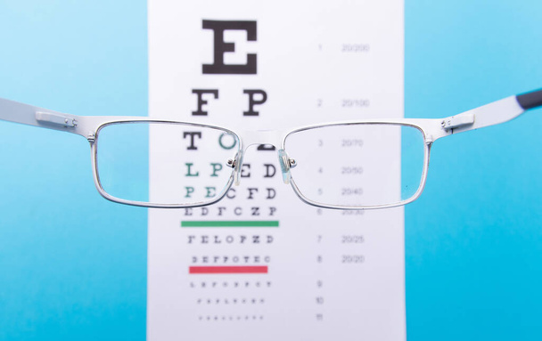 Hand-held glasses, view of the Snellen chart. Blue background - Photo, Image