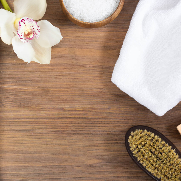 woman body and skincare, massage and bath products, sea salt in bowl, white towel, flower, cacus brush for dry massage on brown wooden background. Beauty blogger cosmetics Copy space Mockup Square - Foto, imagen