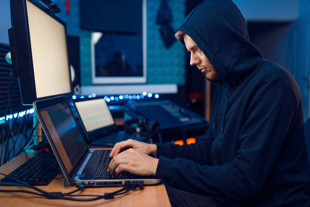 Hacker in der Kapuze sitzen am Laptop, Informationen hacken. Internet-Spion, männliche Programmierer versuchen, ein verschlüsseltes Netzwerk zu hacken - Foto, Bild
