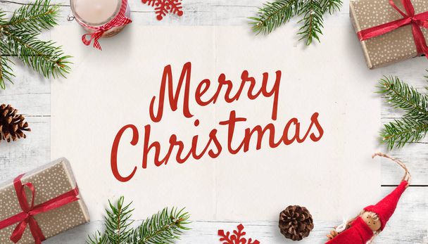 Merry Christmas text on white paper surrounded by Christmas decorations and gifts on white wooden surface. Top view, flat lay composition. Greeting card. - Foto, Imagen