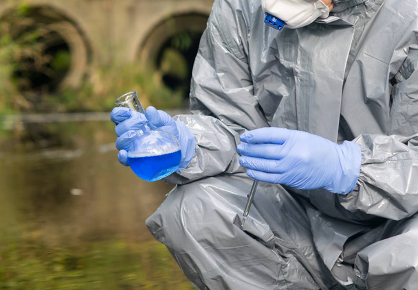 scientist in a protective suit, collects a sample of water in a flask with a blue liquid, close-up, there is a place for the inscription - Photo, image
