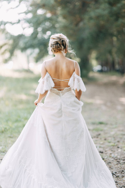 Κομψή τελετή σε ευρωπαϊκό στυλ. Όμορφη νύφη σε λευκό ιπτάμενο φόρεμα στο δάσος.  - Φωτογραφία, εικόνα