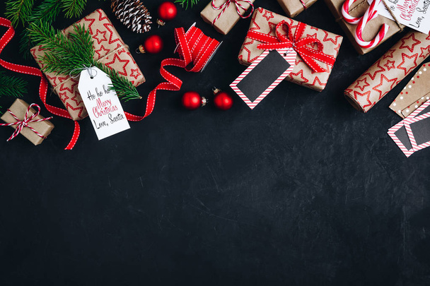 Kerst achtergrond met sparren takken en kegels cadeau dozen met rode strik lint op een donkere betonnen achtergrond.  - Foto, afbeelding