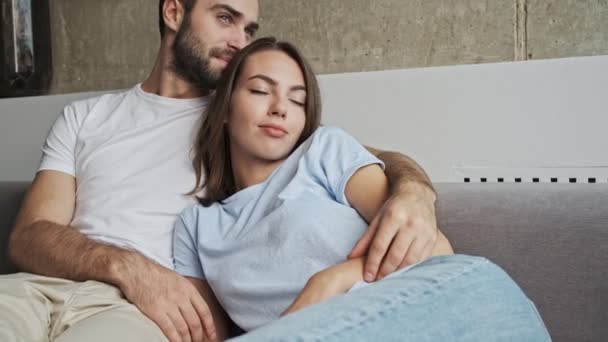 Cute calm young lovely couple hugging with closed eyes and falling asleep while sitting on sofa at home - Materiał filmowy, wideo