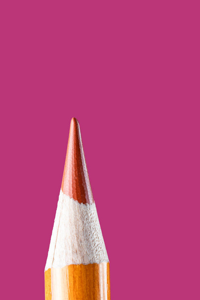 Orange pencil close-up on a pink background. The concept of materials for drawing, training, art therapy. Minimalism, place for text. Vertical photo. - Photo, Image