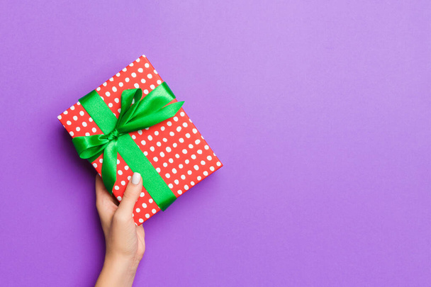 Плоский узор женщины, держащей в руках подарочную упаковку и украшенную бантом на фиолетовом фоне с копировальным пространством. Концепция Рождества и праздника - Фото, изображение