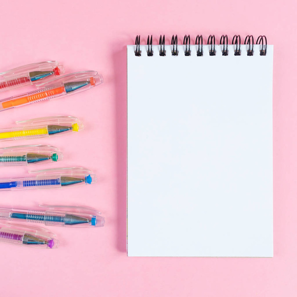 Notebook on a spiral with blank sheets on a pink background. Nearby are the gel pens of rainbow colors. Place for text, minimalism. School stationery concept. - Photo, image