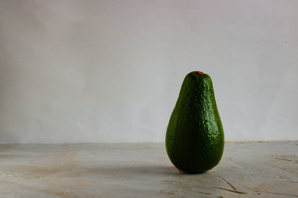 Green fresh avocado standing on white and grey plain empty background. Horizontal with copy space for design and text. Healthy food and diet - Foto, Bild