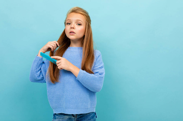kleines Mädchen posiert mit Haarbürste vor blauem Hintergrund  - Foto, Bild