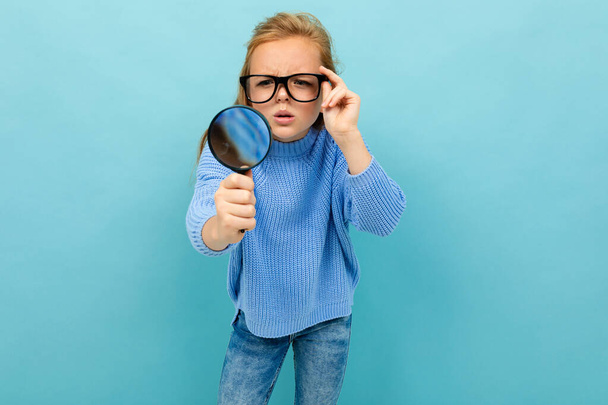 μικρό έξυπνο κορίτσι ποζάρει με γυαλιά και μεγεθυντικό φακό σε μπλε φόντο  - Φωτογραφία, εικόνα
