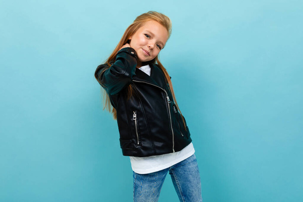 μικρό δροσερό κορίτσι σε μαύρο δερμάτινο μπουφάν θέτει σε μπλε φόντο  - Φωτογραφία, εικόνα
