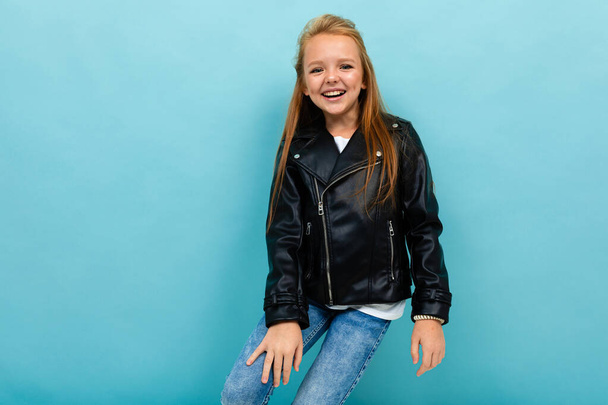 little cool girl in black leather jacket posing against blue background  - Fotoğraf, Görsel