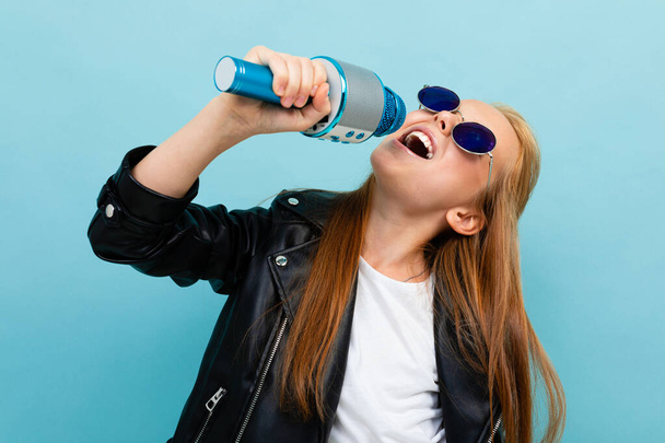 cute little girl in black leather jacket posing with colorful sunglasses against blue background  - Photo, Image