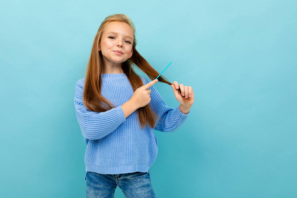 mała dziewczynka pozowanie ze szczotką do włosów na niebieskim tle  - Zdjęcie, obraz
