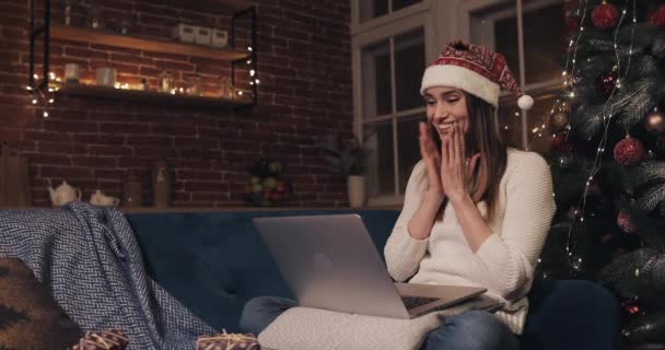 Beautiful Young Caucasian Girl Wearing Santas Hat Sitting near Christmas Tree at Home Background. Woman Using her Laptop Chatting Texting Typing Looking Extremely Happy Smiles - Filmati, video