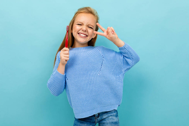 klein meisje poseren met tandenborstel tegen blauwe achtergrond  - Foto, afbeelding