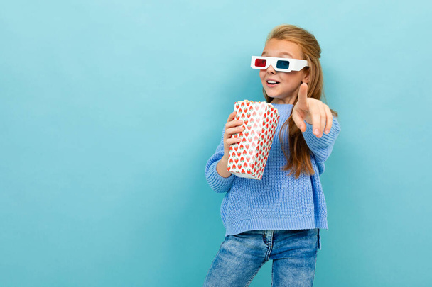 kleines Mädchen posiert mit 3D-Brille und Popcorn vor blauem Hintergrund  - Foto, Bild