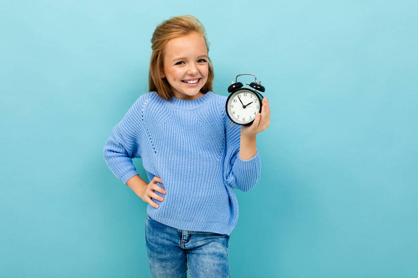 little girl posing with clock alarm against blue background  - Fotografie, Obrázek