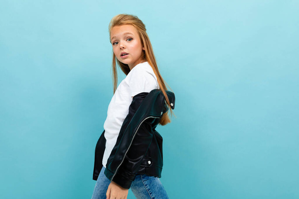 little cool girl in black leather jacket posing against blue background  - Photo, Image