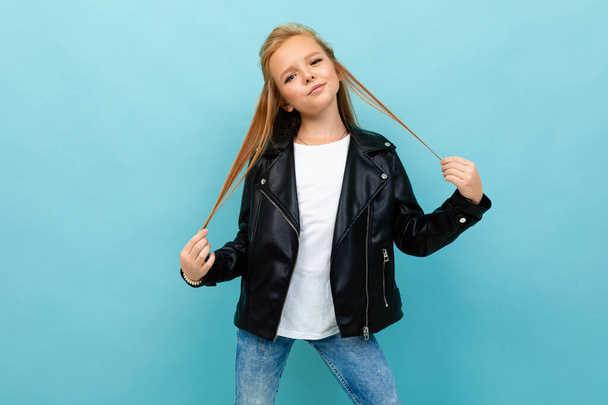 little cool girl in black leather jacket posing against blue background  - Valokuva, kuva