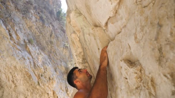 Young muscular man carefully climbing at rock. Strong guy ascending on rock peak making great efforts. Mountaineer on way to mountain top. Concept of extreme sport or active lifestyle. Slow motion - Footage, Video