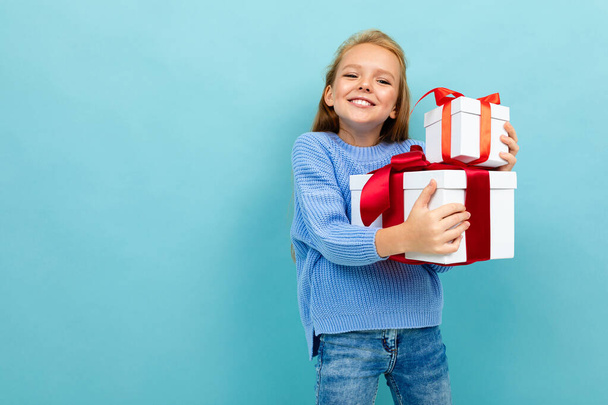 klein meisje poseren met twee geschenken tegen blauwe achtergrond  - Foto, afbeelding