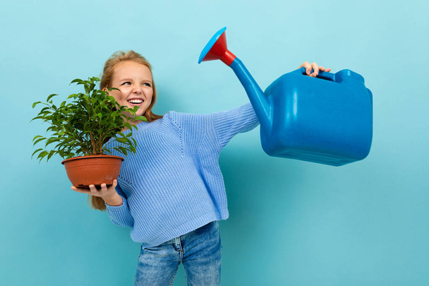 kleines Mädchen posiert mit Gießkanne und Blumentopf vor blauem Hintergrund  - Foto, Bild