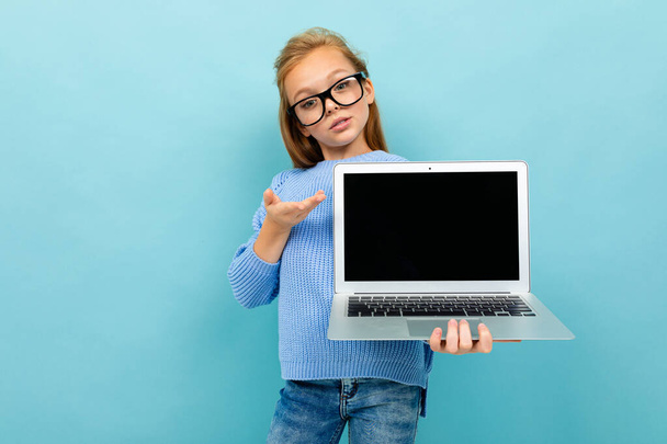 Mavi arka planda gözlük ve dizüstü bilgisayarla poz veren küçük kız  - Fotoğraf, Görsel