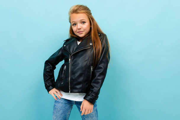 little cool girl in black leather jacket posing against blue background  - Fotoğraf, Görsel