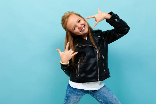 little cool girl in black leather jacket posing against blue background  - Foto, afbeelding