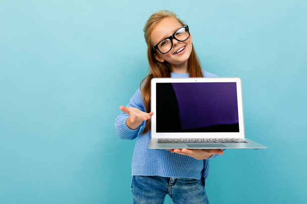 klein meisje poseren met bril en laptop tegen blauwe achtergrond  - Foto, afbeelding
