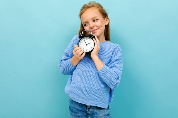 klein meisje poseren met klok alarm tegen blauwe achtergrond  - Foto, afbeelding