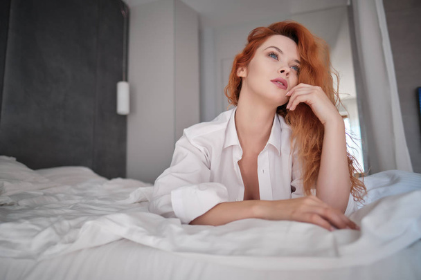 very sensual woman in sexy pose on bed with long natural redhair - 写真・画像