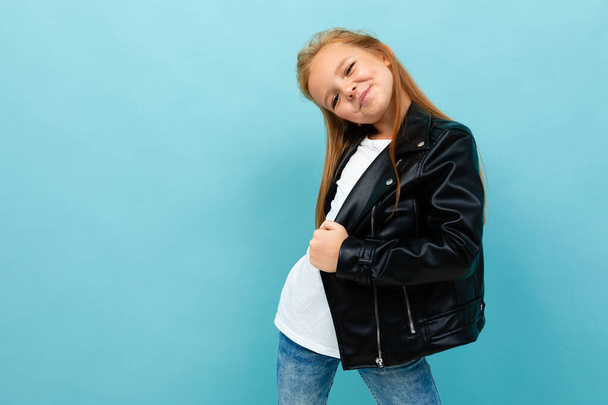 Kleines cooles Mädchen in schwarzer Lederjacke posiert vor blauem Hintergrund  - Foto, Bild