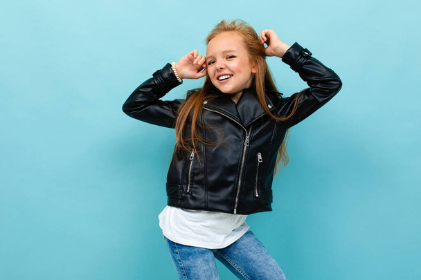 little cool girl in black leather jacket posing against blue background  - Zdjęcie, obraz